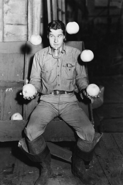 Young man juggling with oranges and balancing a glass under his chin