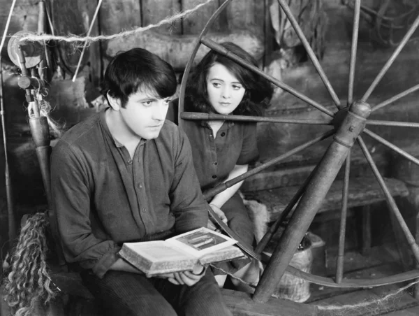 Młody człowiek czytając książkę i młoda kobieta siedzi obok niego — Zdjęcie stockowe
