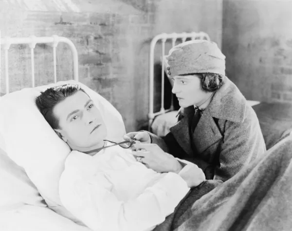 Jovem mulher olhando para uma fechadura de um jovem que está deitado na cama em um hospital — Fotografia de Stock
