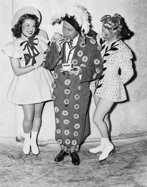 Hombre en un traje hecho de rosquillas de pie entre dos chicas adolescentes —  Fotos de Stock
