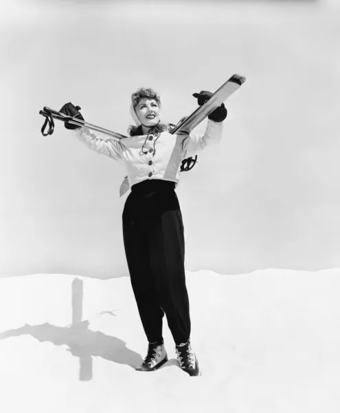 Молодая женщина с лыжами и лыжными палками на плечах — стоковое фото