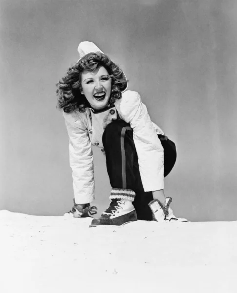Mujer joven arrodillada en la nieve y sonriendo —  Fotos de Stock