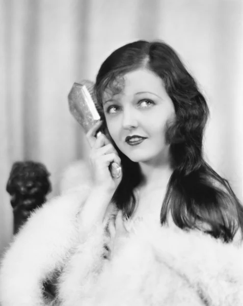 Portret van een jonge vrouw borstelen van haar haren met een haarborstel — Stockfoto