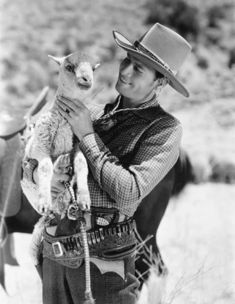 Cowboy carregando um cordeiro e sorrindo — Fotografia de Stock