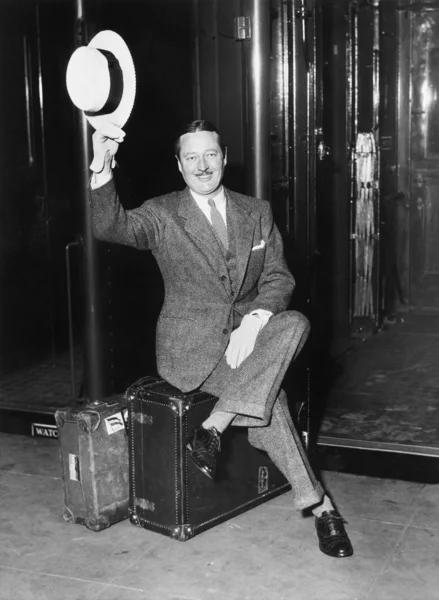 Portrait of a businessman sitting on his suitcases on a platform in front of a train — Stock Photo, Image