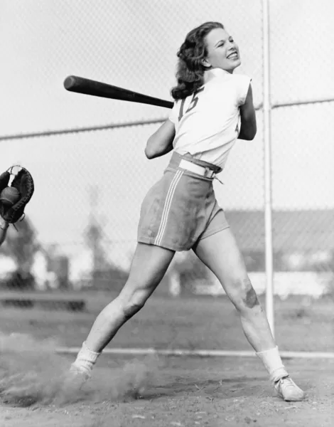 Jovem mulher balançando um taco de beisebol em um campo de beisebol — Fotografia de Stock
