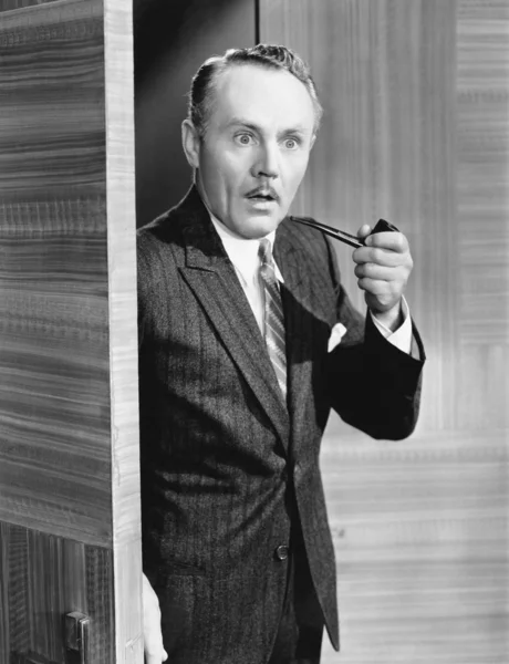 Man holding a pipe and standing at a doorway looking very surprised — Stock Photo, Image