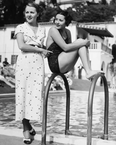 Perfil de una joven sentada en una escalera al lado de la piscina con otra mujer parada detrás de ella —  Fotos de Stock