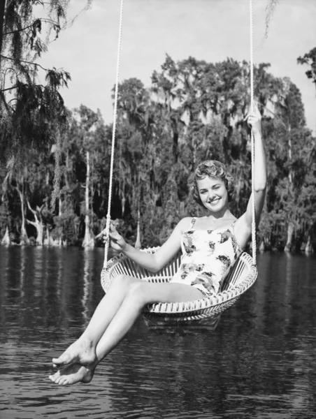 一个年轻女子坐在湖边的秋千上，微笑的肖像 — 图库照片
