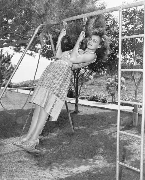 Profil av en ung kvinna som gungar på en gunga i en trädgård — Stockfoto