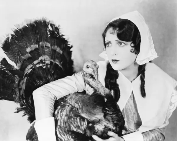 Mujer joven en un capó abrazando a un pavo — Foto de Stock