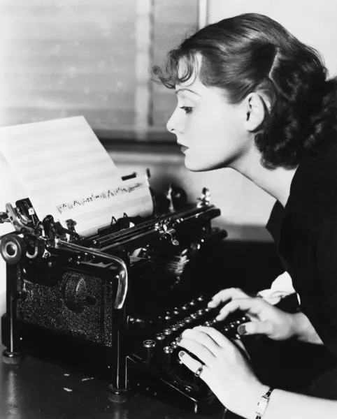 Προφίλ μιας νεαρής γυναίκας πληκτρολογώντας μουσικές νότες με μια γραφομηχανή — Φωτογραφία Αρχείου