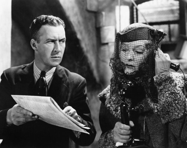 Woman talking on the telephone with a man showing a newspaper to her