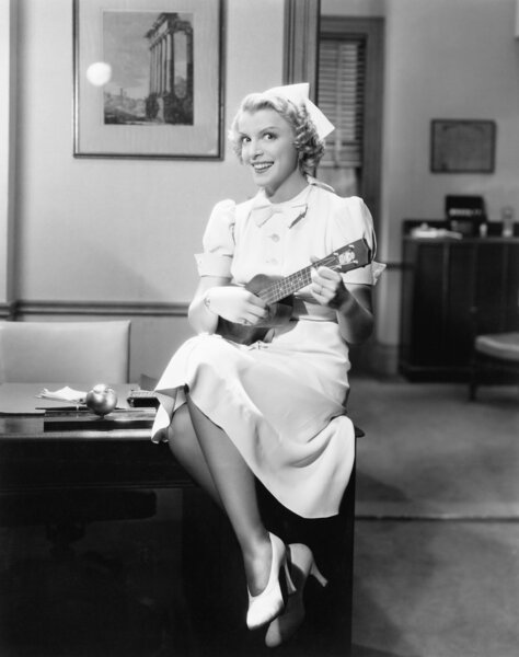 Portrait of a female nurse sitting on a table and playing a guitar