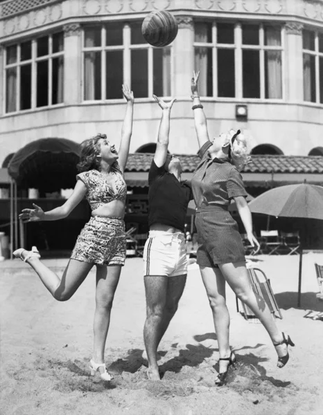 Tre unga kvinnor leker med en boll på stranden — Stockfoto