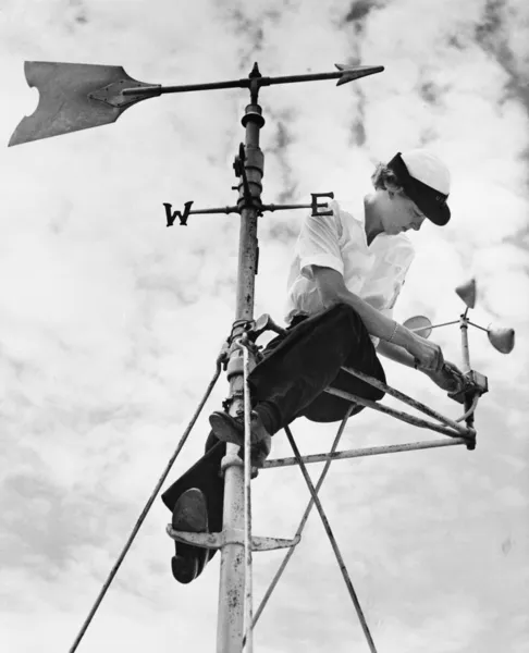 Low angle view of a young woman mending a weather vane — Stock Photo, Image