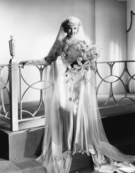 Νεαρή γυναίκα στέκεται στο γαμήλιο φόρεμα και κρατώντας ένα μπουκέτο λουλούδια — Φωτογραφία Αρχείου