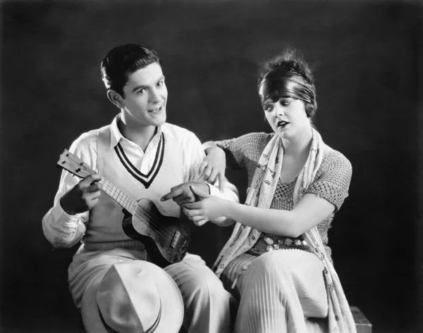 Jonge man met een gitaar met een jonge vrouw die hem onderwijzen hoe te spelen — Stockfoto