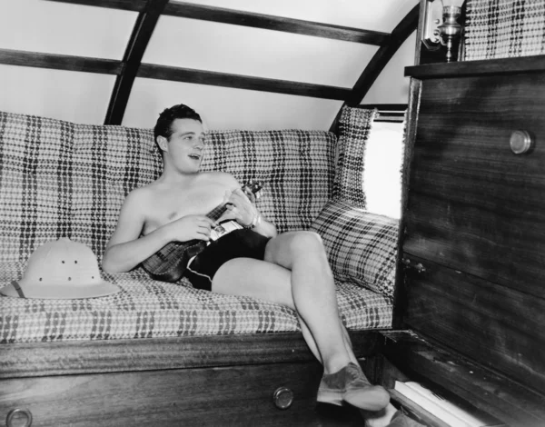 stock image Young man sitting on a couch and playing a guitar