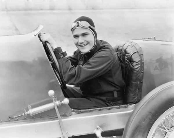 Молодой человек, сидящий в гоночной машине с широкой улыбкой — стоковое фото