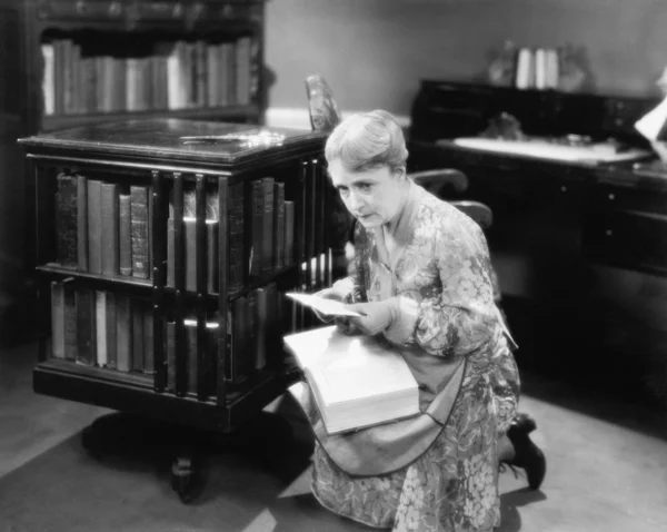 Mujer arrodillada con un libro en su biblioteca encontrando una carta —  Fotos de Stock