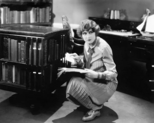Mujer arrodillada con un libro en su biblioteca encontrando una carta — Foto de Stock