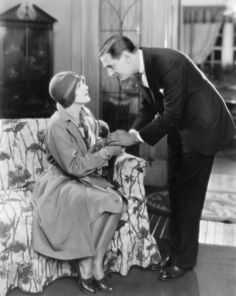 Man bending over a woman sitting on a sofa