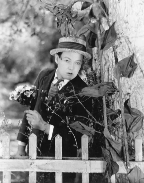 Молодий чоловік ховається за деревом з букетом квітів в руках — стокове фото