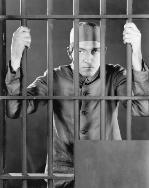 Häftling hinter Gittern sieht wütend und traurig aus — Stockfoto