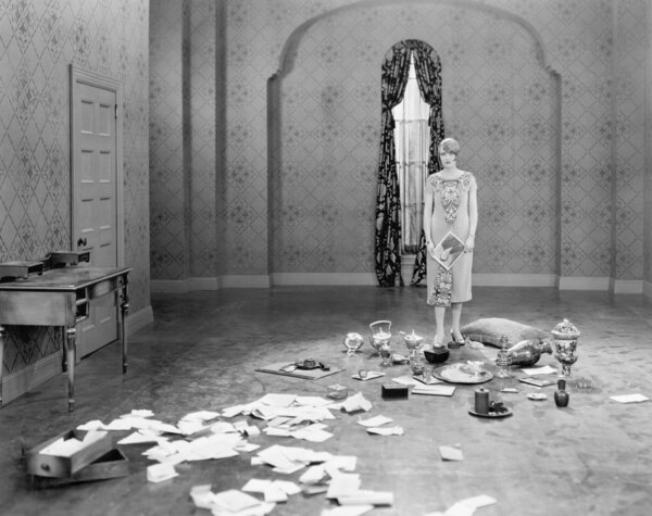 Woman standing in an empty room scattered with letters