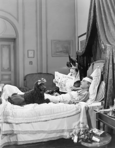Mulher e poodle sentados ao lado de um homem ferido na cama — Fotografia de Stock