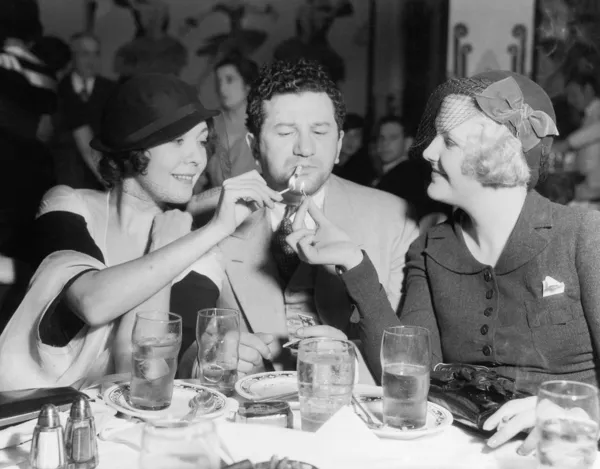 Two women lighting a cigarette for a man — Stock Photo, Image