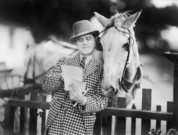 Un uomo appoggiato ad un recinto che legge una lettera al suo cavallo — Foto Stock