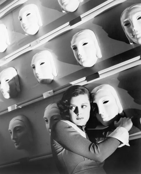 Kvinna som tittar rädd håller på en mask på väggen i masker — Stockfoto