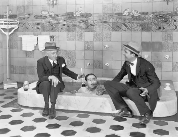 Dois homens sentados à beira de uma banheira em ternos e esfregando um amigo de volta — Fotografia de Stock