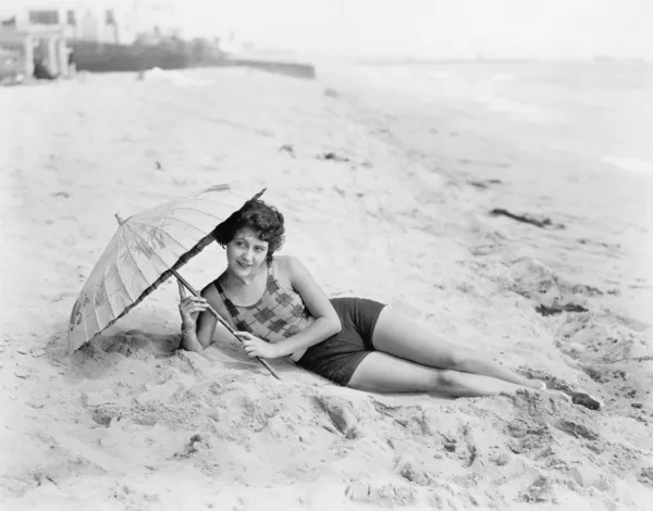 Kobieta, leżąc na plaży z parasolem — Zdjęcie stockowe