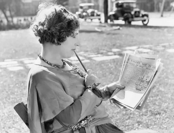 Kobieta z ołówkiem w jej usta, czytania gazety — Zdjęcie stockowe