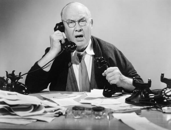 Man on multiple telephones looking angry