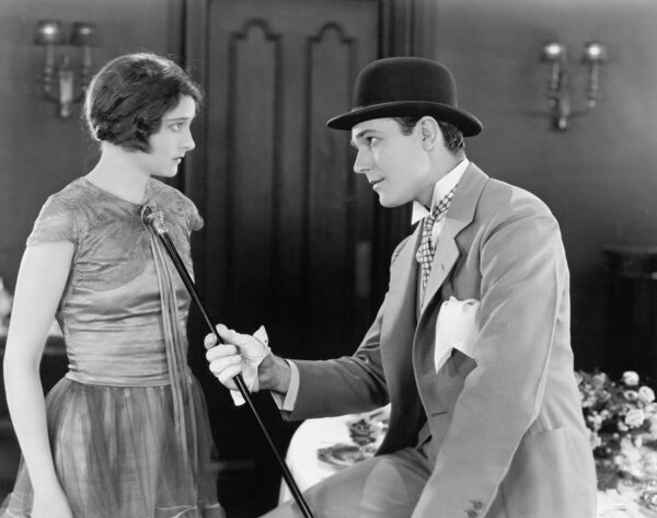 Man pushing his walking stick against a surprised looking woman