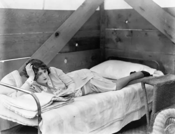 Frau streckt sich auf einem Kinderbett aus und liest ein Buch — Stockfoto