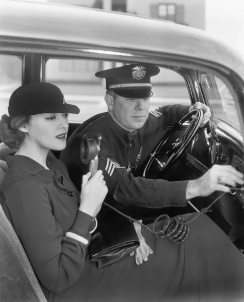 Woman sitting next to a policeman in his car holding a microphone in her hand — Stock Photo, Image