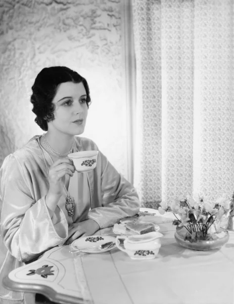 Mujer sentada en una mesa con una taza de té en la mano — Foto de Stock