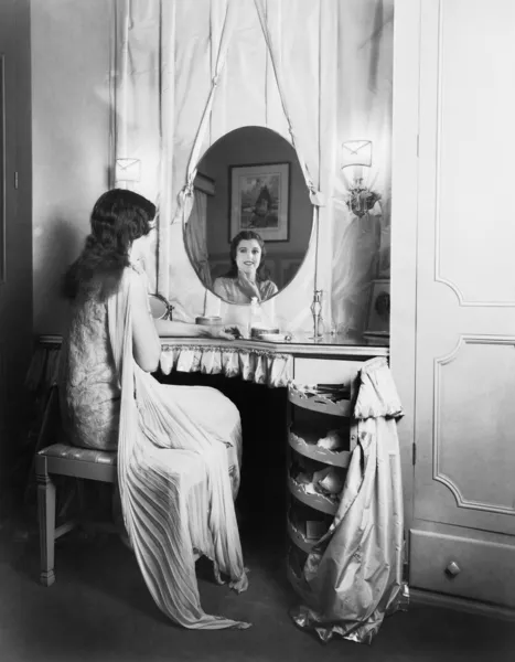 Жінка сидить за столом марнославства, посміхаючись у дзеркало — стокове фото