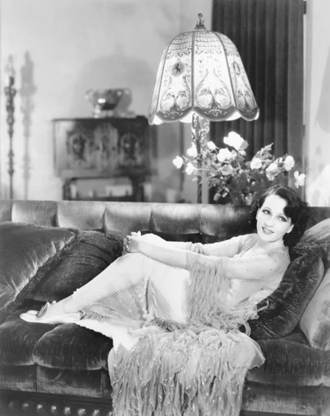 Γυναίκα περιτυλίγματος τα χέρια της γύρω από τα γόνατα, Φωλιασμένο σε έναν καναπέ — Φωτογραφία Αρχείου