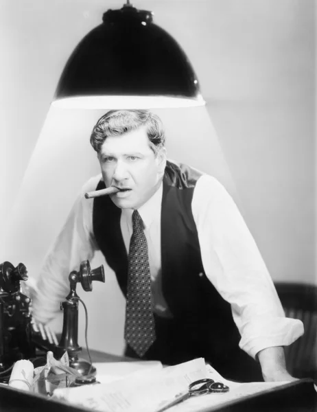 Mann lehnt sich über einen Schreibtisch, auf dem ein Deckenlicht leuchtet — Stockfoto