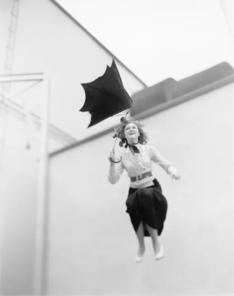 Молодая женщина сдувается, прыгая с крыши с зонтиком — стоковое фото