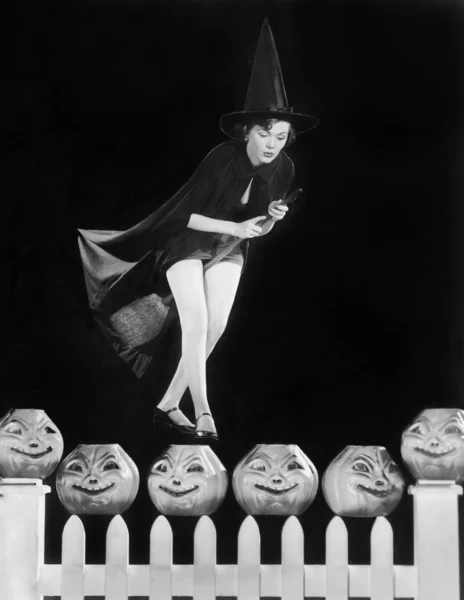 Young witch hovers on her broom, eyeing which pumpkin to choose — Stock Photo, Image