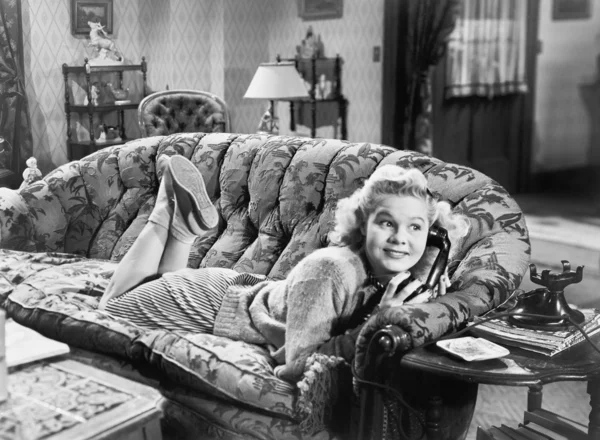 Ung kvinna liggande på en soffa i ett vardagsrum och pratar i telefonen — Stockfoto
