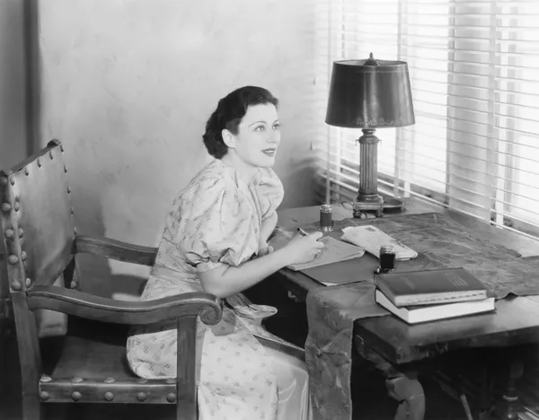 Ung kvinna sitter vid hennes skrivbord skriva ett brev — Stockfoto