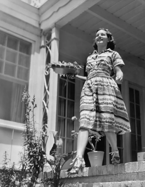 Jonge vrouw lopend onderaan de stappen van haar terras met een plaat in haar handen — Stockfoto